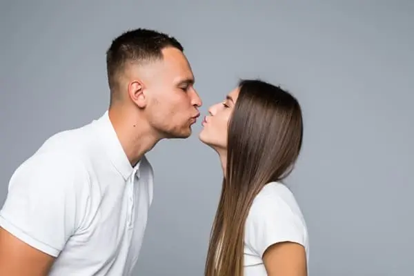 um homem branco e uma mulher branca vestidos com camiseta branca fazendo movimento para se beijar