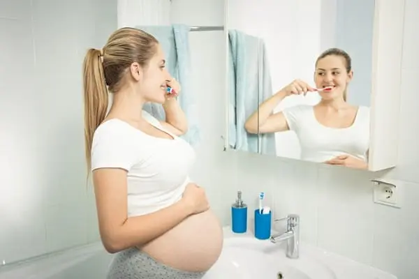 mulher branca gravida escovando os dentes no banheiro cuidando da sua higiene bucal na gravidez