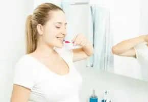 mulher branca escovando os dentes no banheiro cuidando da sua higiene bucal na gravidez